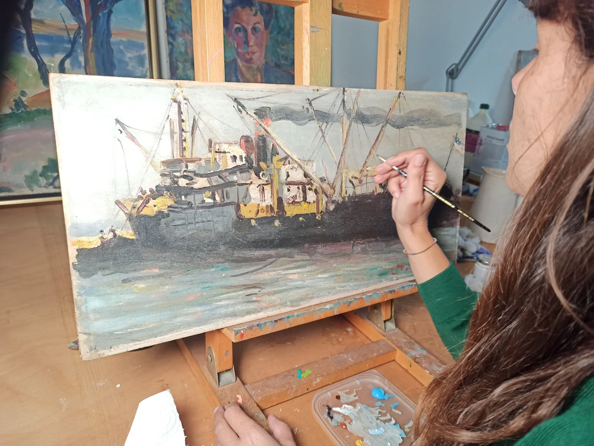 Nettoyage localisé au coton-tige sur la surface d’un tableau ancien à l’atelier.